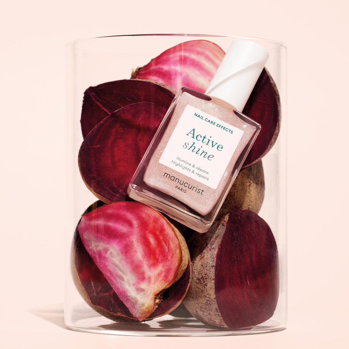 Un flacon de soin des ongles Manucurist Active™ Shine Opal repose sur des betteraves rouges et roses tranchées dans un récipient en verre transparent, sur un fond beige clair.