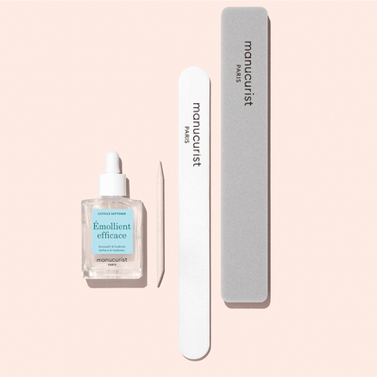 The Manucurist Nail Prep Set—including a cuticle oil bottle with dropper, wooden cuticle stick, white nail file, and gray emery board buffer, all essential for nail prep—is arranged neatly on a light pink background.