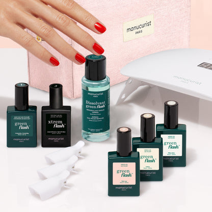 A hand with red-painted nails reaches toward a Manucurist Starter Kit - Soap Nails LED Gel Polish, which includes bottles, remover, white clips, and an LED lamp.
