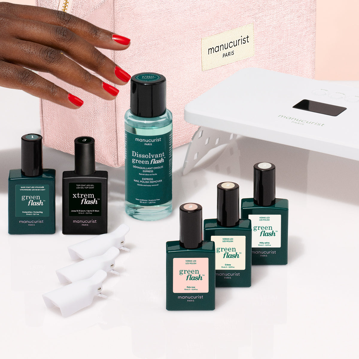 A hand with red-painted nails next to a Starter Kit - Soap Nails LED Gel Polish, featuring a bottle of nail polish remover, four white nail clips, and a portable LED lamp for an ultra-glossy manicure.