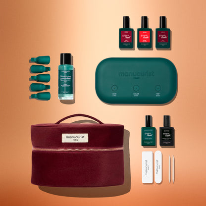 Vue à plat du coffret kit de démarrage Green Flash™ de Manucurist : flacons de vernis, dissolvant, accessoires à capuchon vert, lampe turquoise pour les ongles, limes et pince à épiler sont disposés près d’une trousse zippée bordeaux, sur un fond pêche en dégradé. De quoi réaliser une manucure digne d’un salon à la maison.
