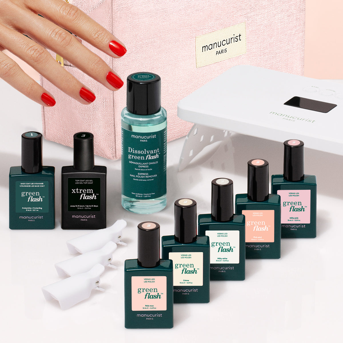 A hand with red-painted nails reaches toward a Super Starter Kit - Soap Nails LED Gel Polish, with bottles, remover, an LED lamp, and clips arranged in front of a pink cosmetic bag to achieve an ultra-glossy manicure.
