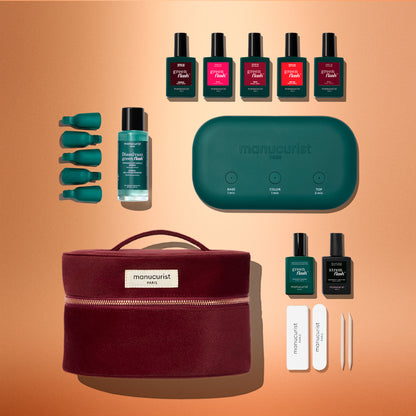The Manucurist Green Flash™ Super Starter Kit Gift Set features nail polish bottles, remover caps, nail files, a green LED lamp, and manicure tools arranged neatly on an orange background—everything you need for a salon-style manicure at home with long-lasting results.