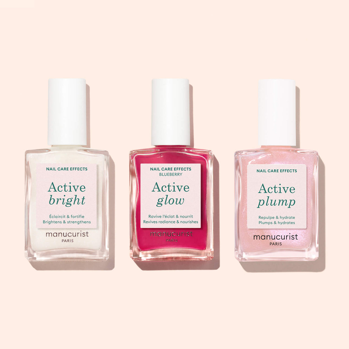 Trois flacons de soins pour les ongles Manucurist — Active™ Bright, Active Glow et Active Plump — posés côte à côte sur une surface rose clair. Chaque flacon présente un liquide de couleur différente et des étiquettes blanches, mettant en valeur cette collection de vernis biosourcés et de formules fortifiantes nourrissantes de Manucurist.