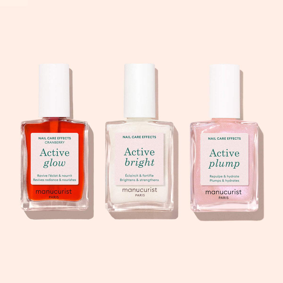 Trois flacons de soins pour ongles Manucurist — Active™ Glow Cranberry (rouge), Active Bright (blanc) et Active Plump (rose) — sont présentés côte à côte sur un fond beige clair, mettant en valeur l&