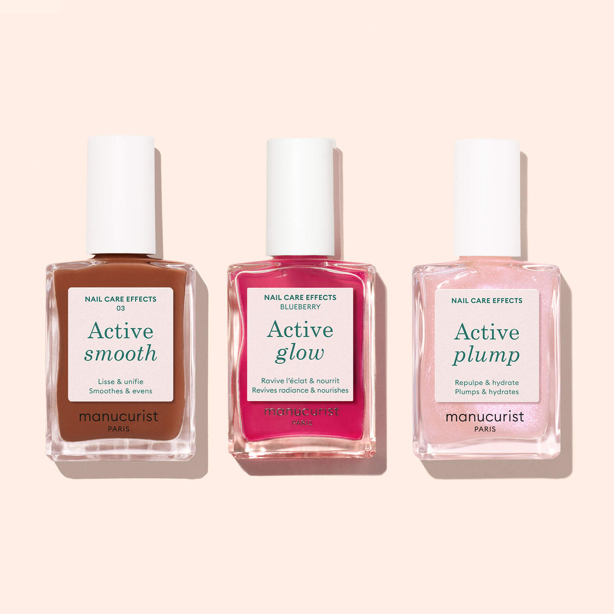 Trois flacons de vernis Manucurist Active Smooth 03 se détachent sur un fond rose clair. Les étiquettes indiquent « Active Smooth », « Active Glow » et « Active Plump » — un trio élégant pour votre routine de soin des ongles.