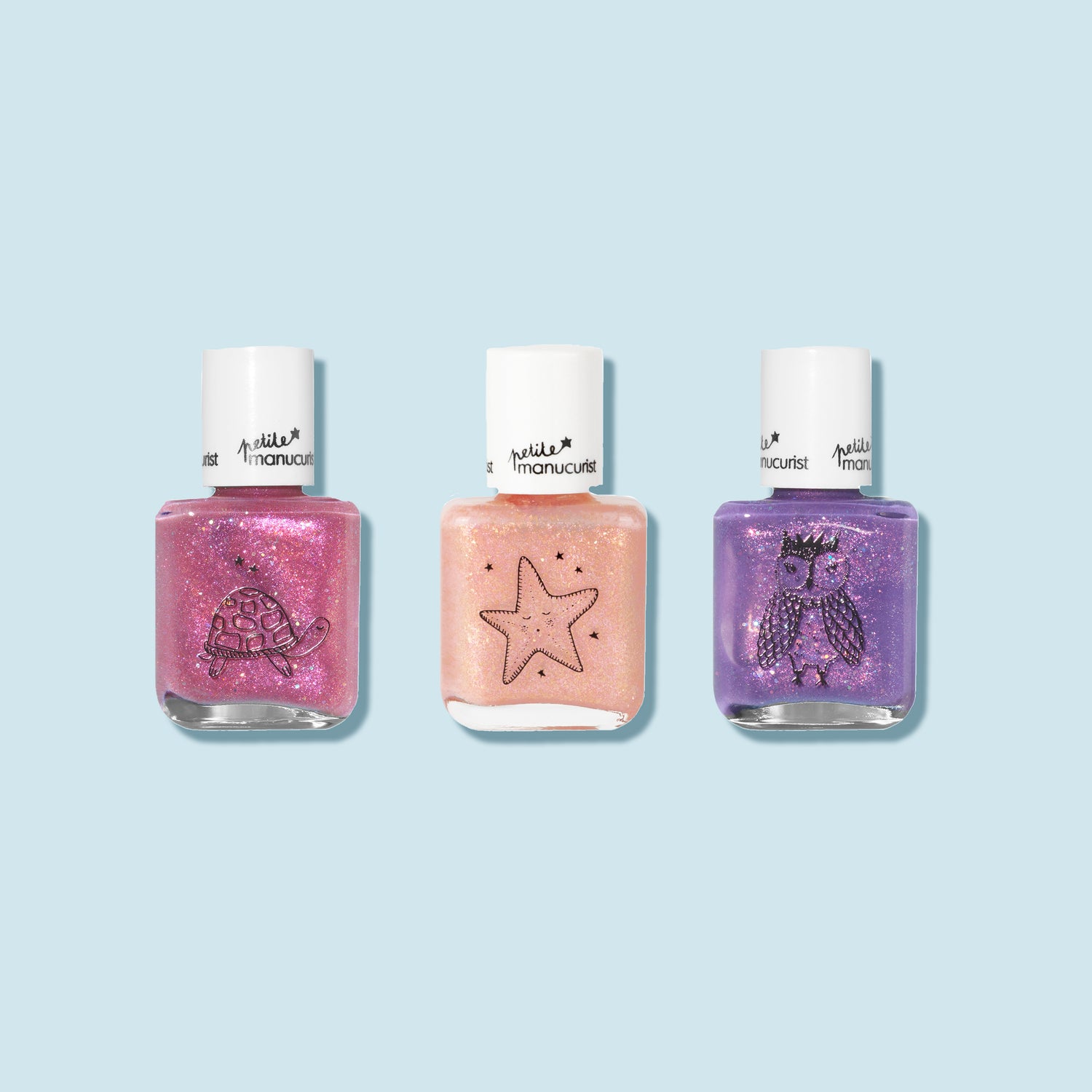The Manucurist Customizable 3-pack Petite Manucurist features kids nail polishes—pink with a turtle, peach with a star, and purple with an owl—displayed on a light blue background.