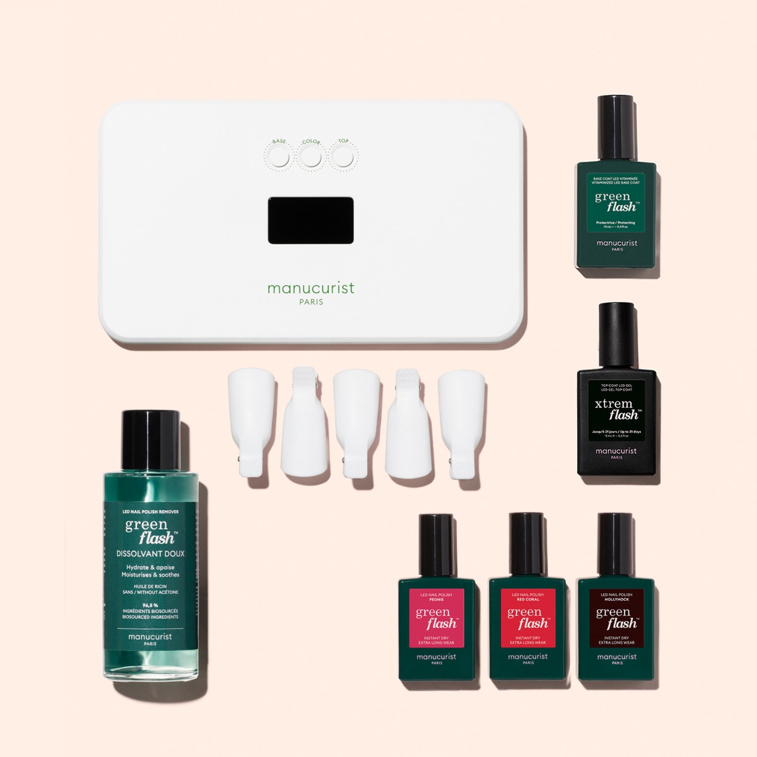 The Manucurist Starter Kit includes an LED lamp, nail polish remover, four red and pink polishes for a glossy manicure, two green bottles (one is a vitaminized base coat), and four white clips, all shown on a light pink background.