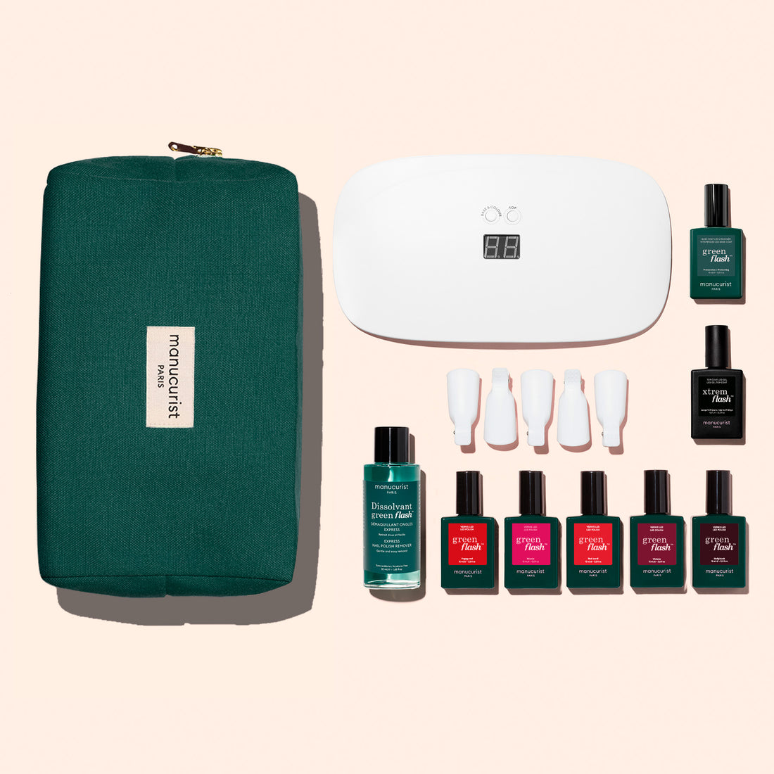 The Manucurist Super Starter Kit features a green zippered pouch, white LED nail lamp, four nail polishes (including a vitaminized base), nail polish remover, and four white tools arranged on a light background.