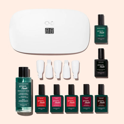 The Manucurist Super Starter Kit includes a white LED lamp, nail clips, remover bottle, six colorful long-lasting gel polishes, and two black top and base coat bottles—all set against a light pink background for an ultra-glossy manicure.