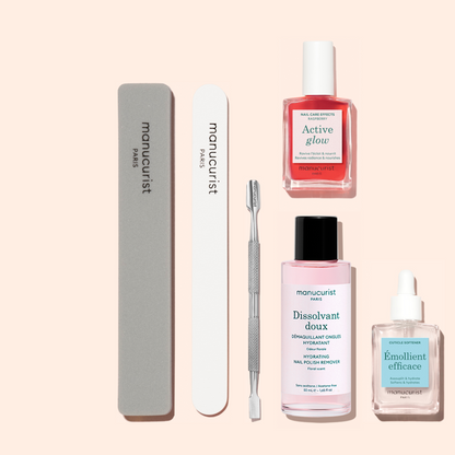 The Manucurist Active Discovery Kit—featuring two nail files, a cuticle pusher, nail polish remover, nail care serum, and a cuticle softener—is artfully arranged on a pale pink background to enhance your manicure results and elevate your nail care routine.