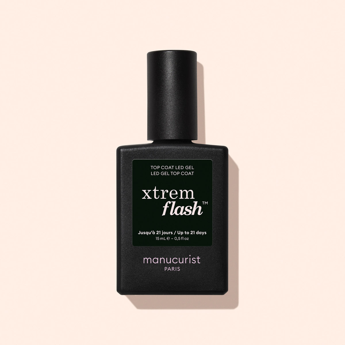 Un flacon noir de Top Coat Gel Manucurist Xtrem Flash™ est posé sur un fond rose pâle, avec une étiquette vert foncé au texte blanc et jaune mettant en avant un retrait express et une tenue impeccable.