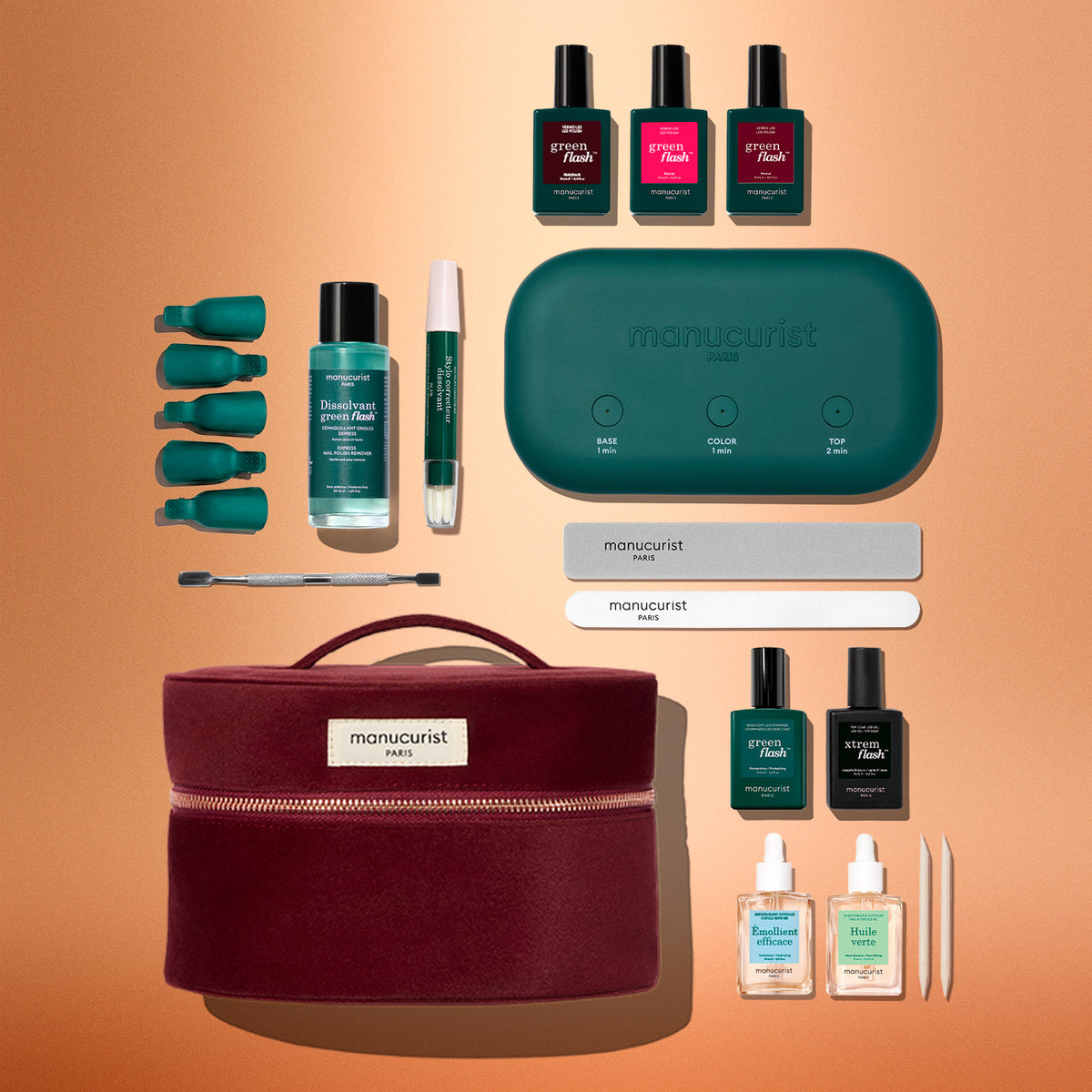 Achieve a salon-quality manicure at home with the Manucurist Green Flash™ Ultimate Kit Gift Set, which includes nail polishes, remover clips, nail files, a green manicure tool, a burgundy carrying case, a green LED lamp, remover bottles, a brush, and a cuticle pen—all beautifully displayed against a peach backdrop.