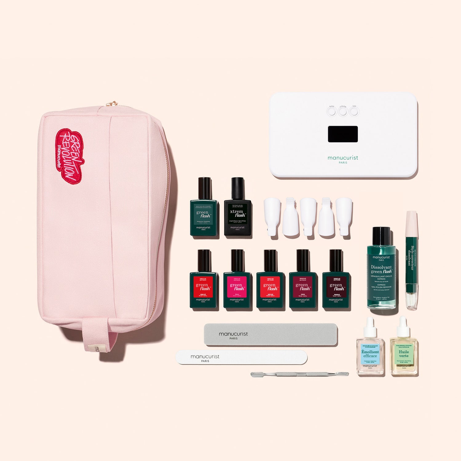 The Manucurist Super Ultimate Kit includes a pink pouch, white LED nail lamp, six Green Flash gel polishes, nail care tools, four nail clips, two vitaminized base coats, and a green gel pen—all arranged on a beige background.