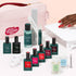 The Manucurist Super Ultimate Kit, featuring Green Flash gel polish, remover, nail oils, files, and a vitamin-enriched base coat with a pink bag. A hand with red nails showcases an ultra-glossy look under a white LED lamp.