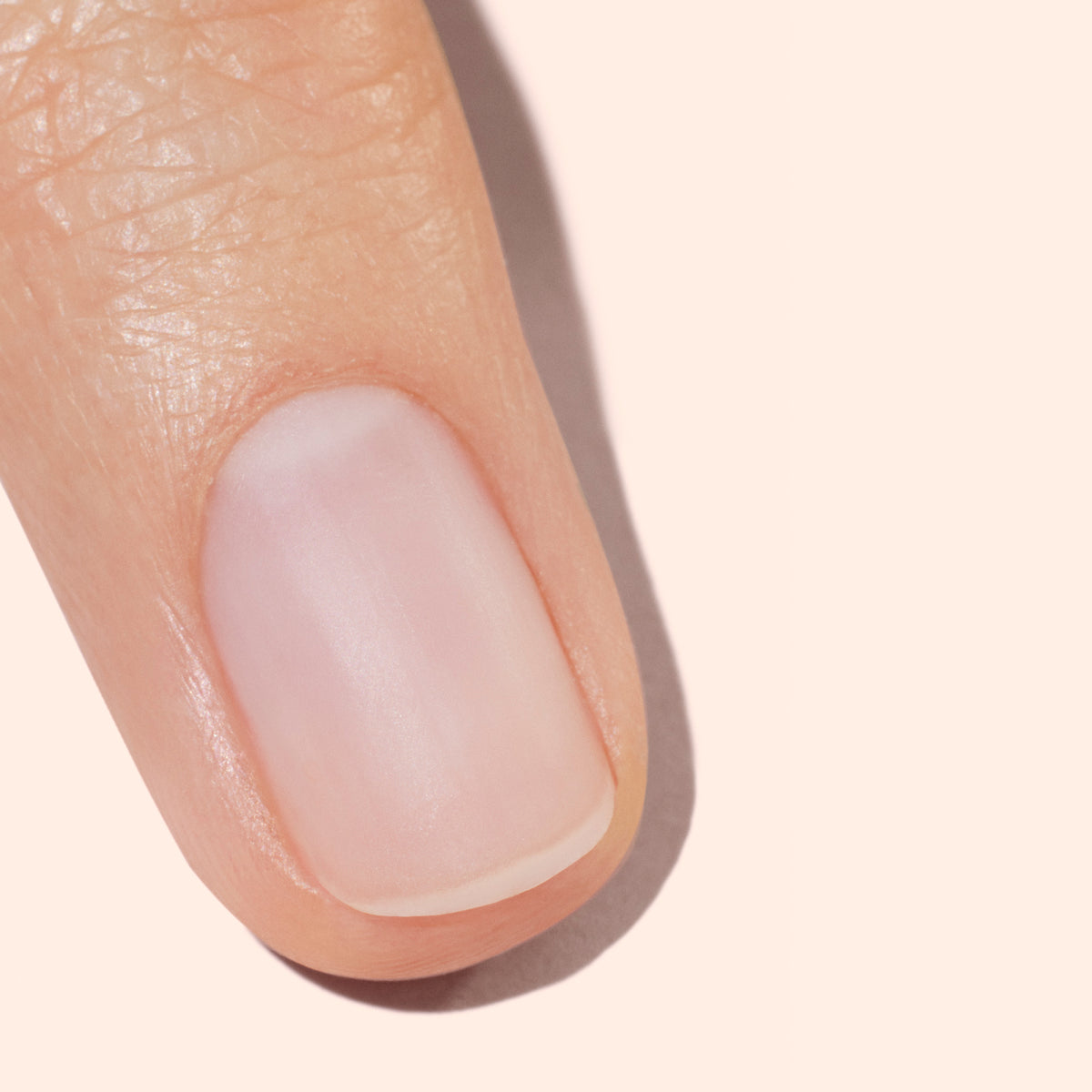 Gros plan d’un ongle propre et soigné sur un doigt à la peau lisse et saine, photographié sur un fond beige clair.