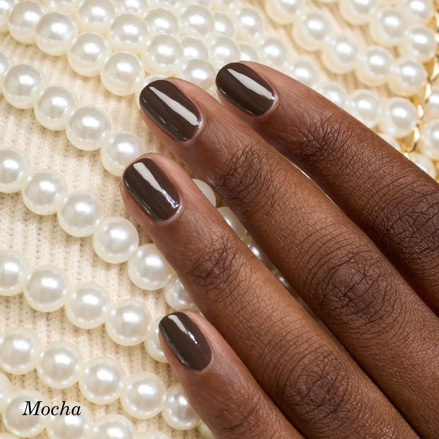 A hand with neatly manicured mocha-colored nails rests on strands of white pearls arranged on a cream knit fabric. The word Mocha appears in the bottom left corner.