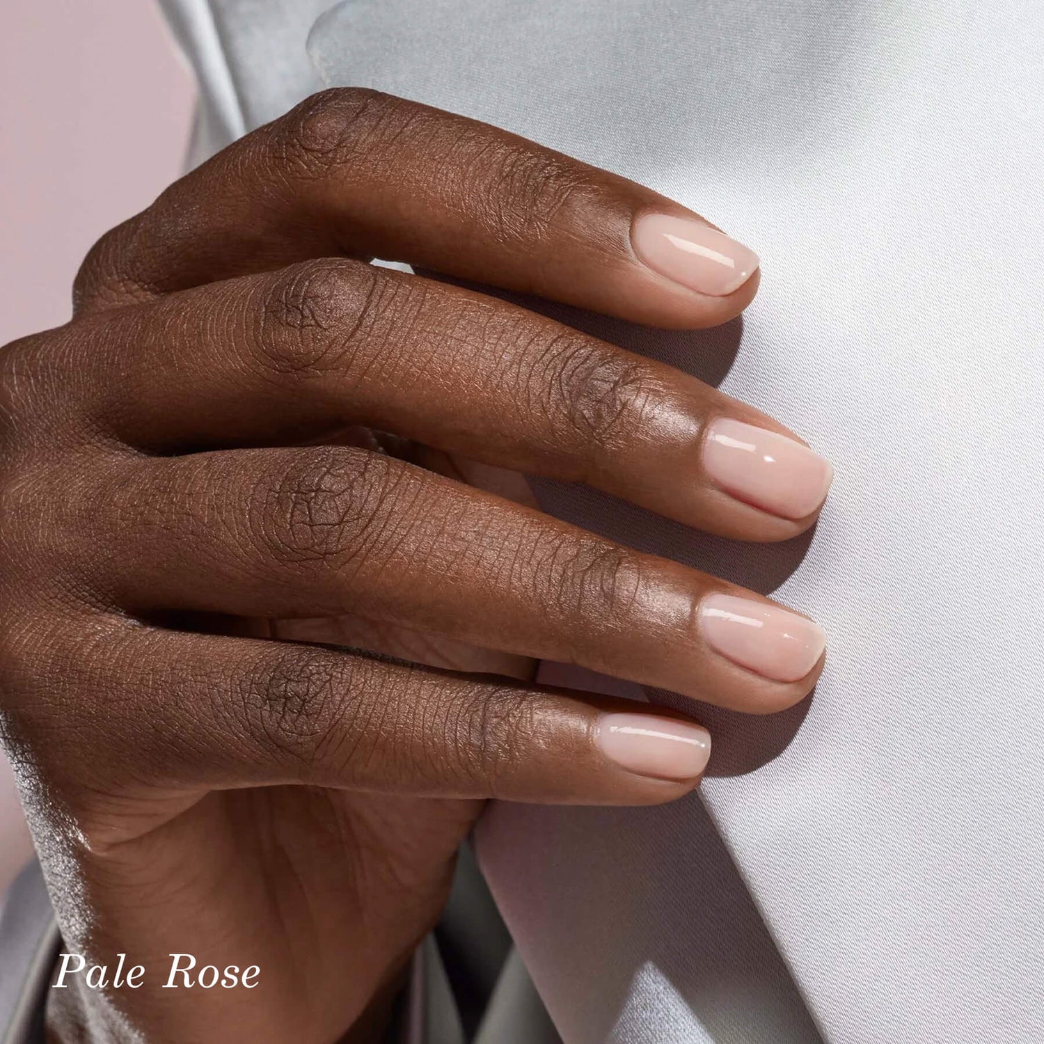 A hand with neatly manicured nails painted a pale rose color rests against a light gray fabric. The words Pale Rose appear in the bottom left corner.
