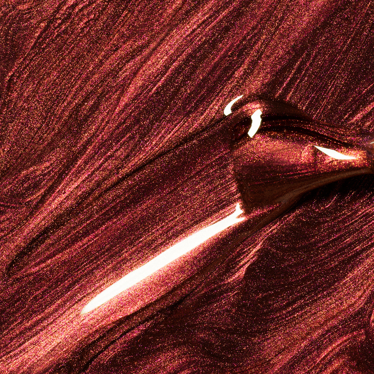 Close-up of Manucurist’s Utopia, a shimmering metallic crimson nail polish, spread smoothly with a brush to create glossy, textured streaks that beautifully reflect light.