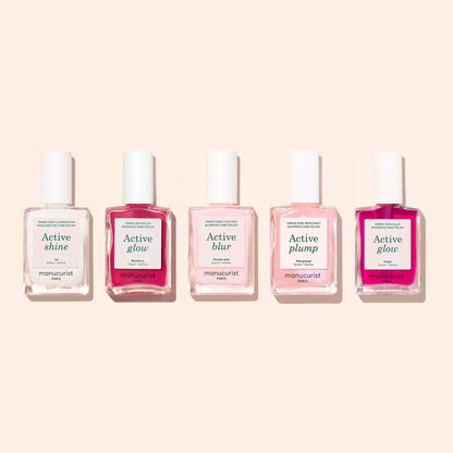 Five bottles of Manucurist nail treatments are lined up on a light beige background, each showcasing different labels: Active™ Shine Icy, Active Glow, Active Blur, and Active Plump. Perfect for your nail care routine, these formulas combine the illuminating effect of a nail polish with the strengthening power of a nourishing treatment.