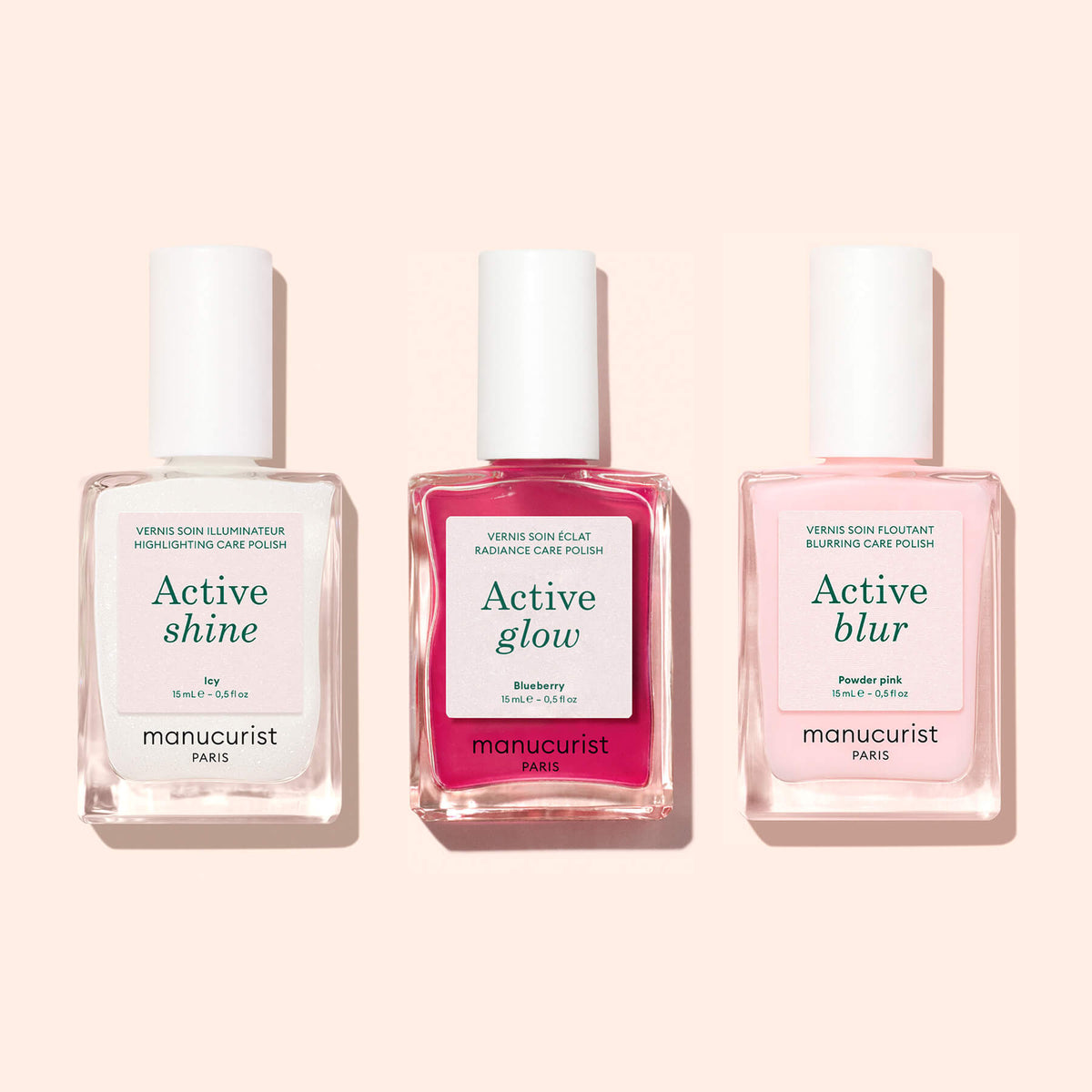 Three nail polish bottles labeled Manucurist Active™ Shine Icy, Active Glow, and Active Blur stand side by side against a light pink background. Perfect for your nail care routine, the clear, red, and pale pink bottles with white labels and caps feature formulas that work as both illuminating nail polishes and nail strengtheners.