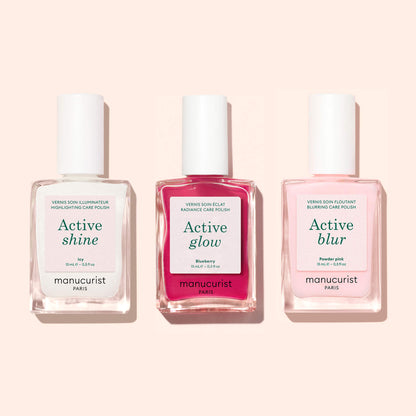 Three nail polish bottles labeled Manucurist Active™ Shine Icy, Active Glow, and Active Blur stand side by side against a light pink background. Perfect for your nail care routine, the clear, red, and pale pink bottles with white labels and caps feature formulas that work as both illuminating nail polishes and nail strengtheners.