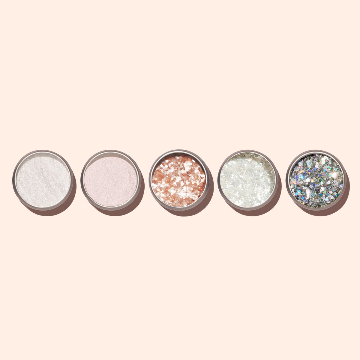 Cinq contenants ronds de Blush Biodegradable Glitter de Manucurist, présentant différentes poudres irisées et pailletées, dont un rose pâle idéal pour le Nail Art, sont alignés sur un fond beige clair.