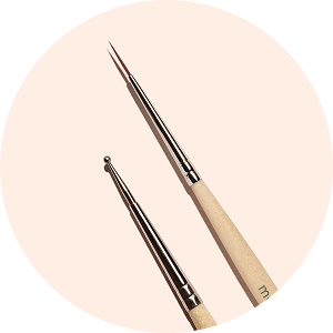 Deux outils de Nail Art aux manches beiges sont présentés sur un fond clair. L’un possède une pointe de pinceau fine et pointue, l’autre une petite pointe à bille métallique pour réaliser des pois.
