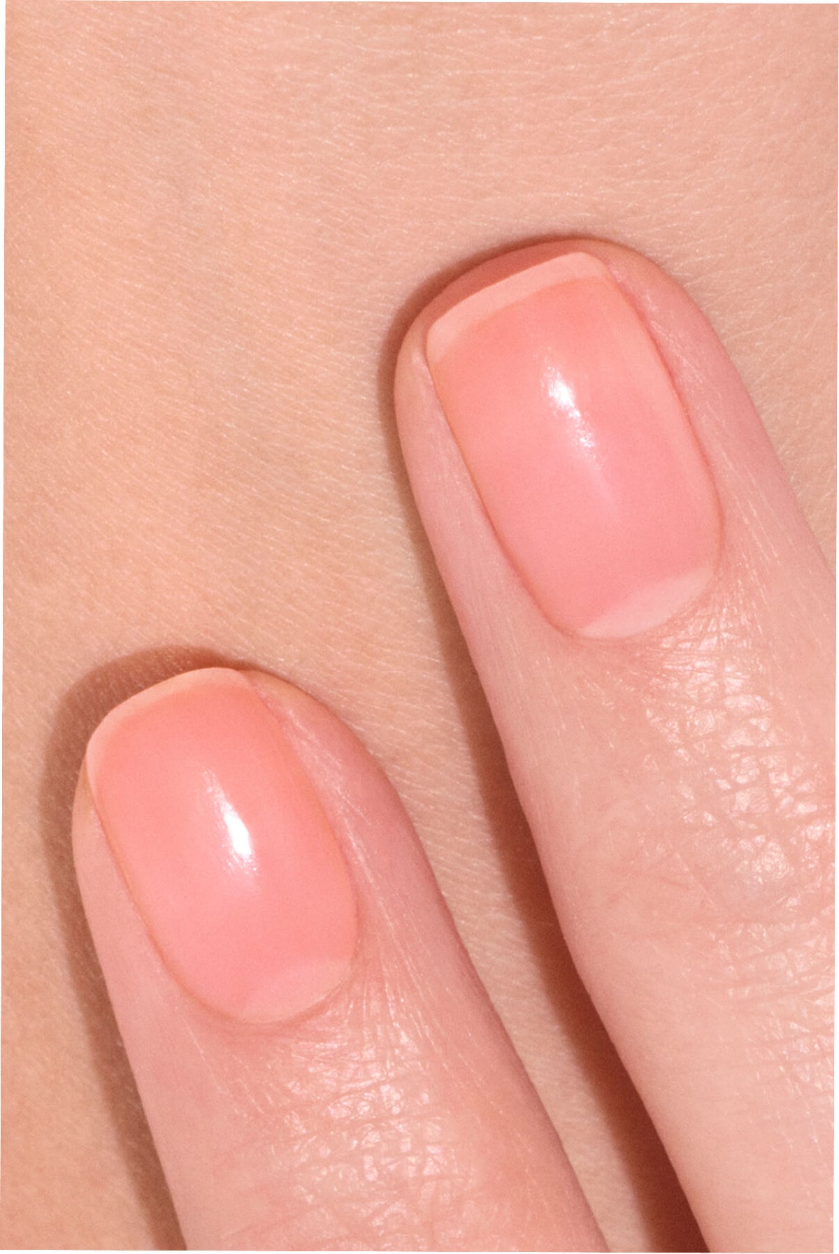 Deux doigts aux ongles soigneusement manucurés, vernis d'un rose clair brillant, délicatement posés sur une peau lisse.