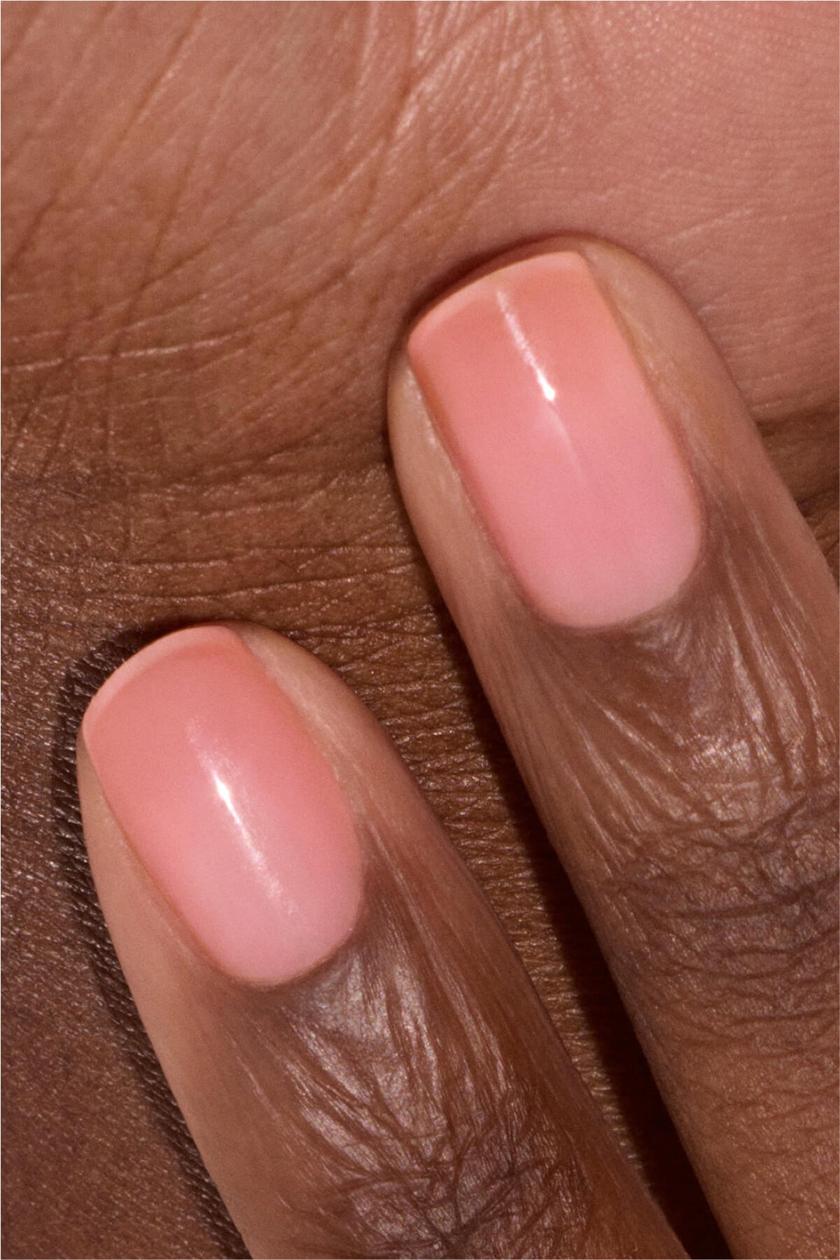 Gros plan de deux doigts aux ongles soigneusement manucurés, peints d'un rose clair brillant, sur fond de peau brune.