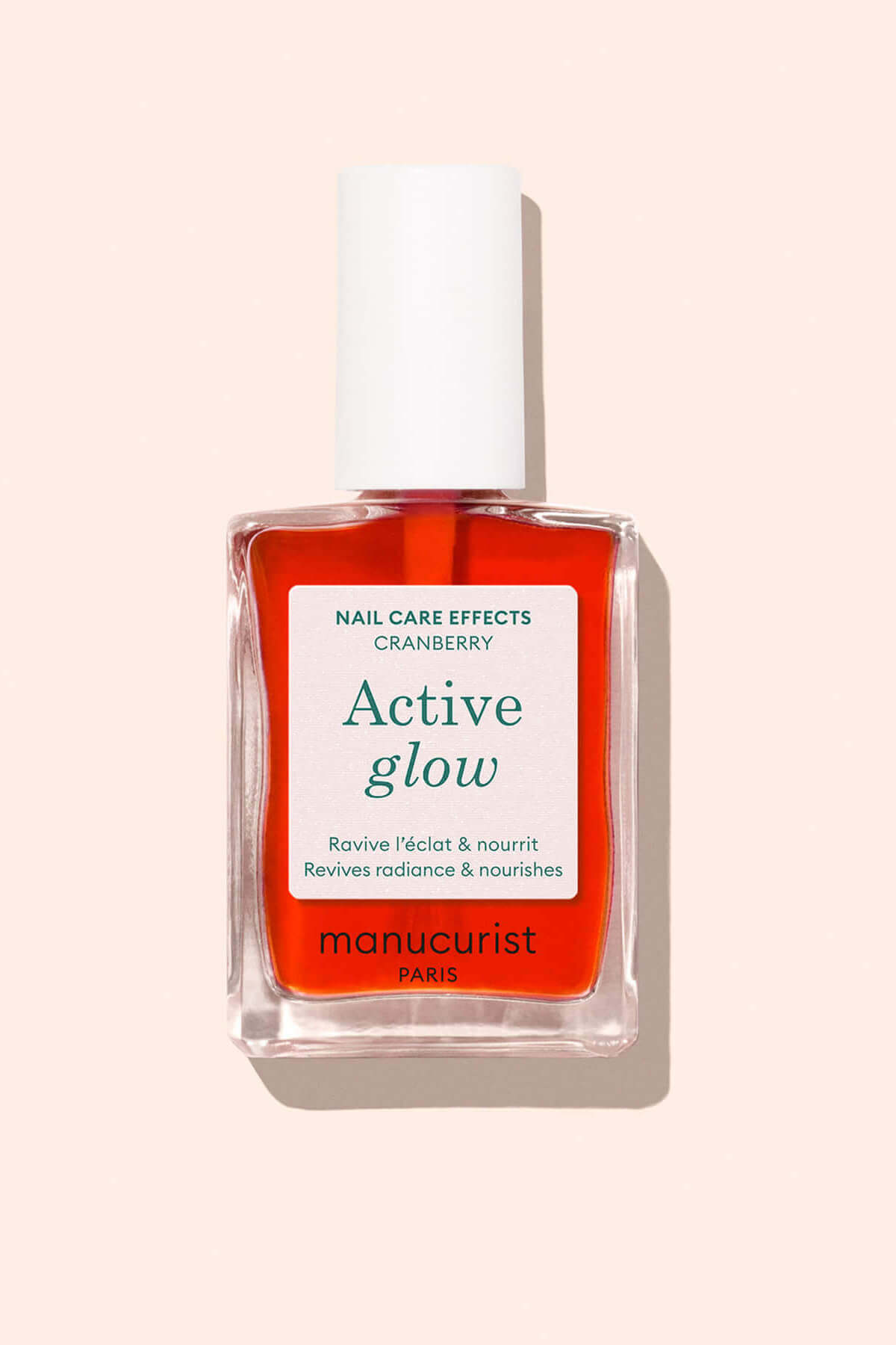 A clear glass bottle of red manicure polish labeled manucurist PARIS Active Glow with white cap, against a light pink background. The label mentions Nail Care Effects Cranberry and Revives radiance  nourishes.