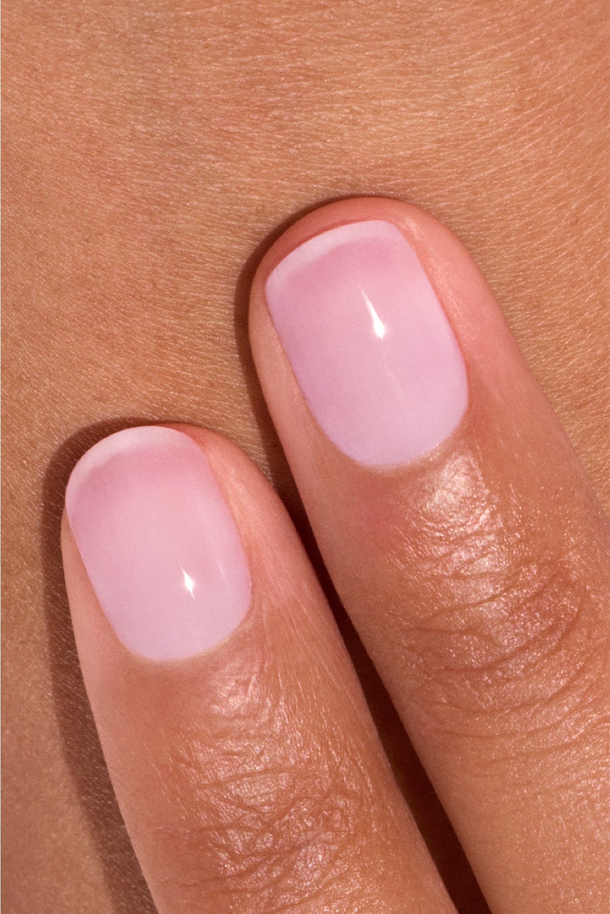 Gros plan sur deux doigts aux ongles courts et soigneusement manucurés, vernis d'une teinte rose pâle brillante, sur une peau claire à mate.