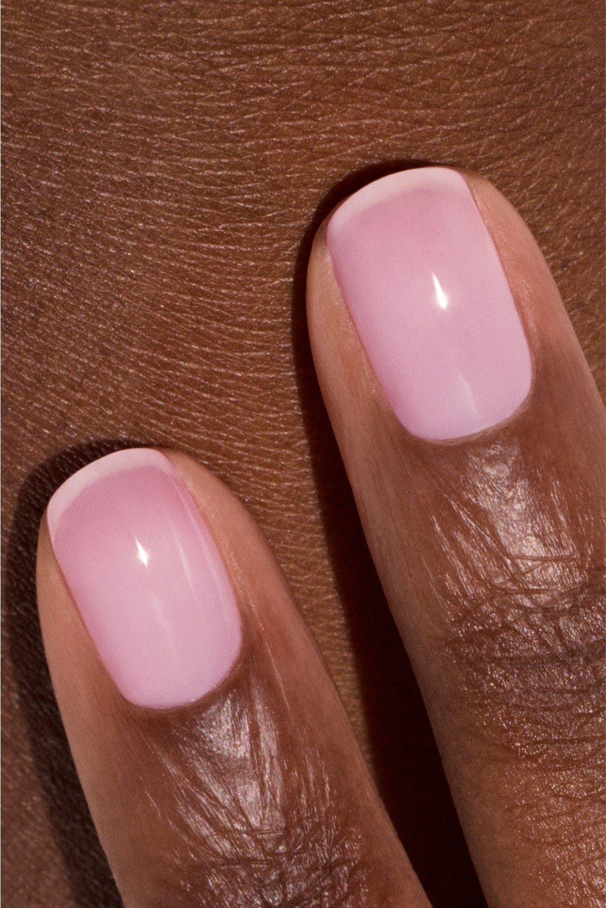 Gros plan sur deux doigts aux ongles courts et soigneusement manucurés, vernis d'un rose clair brillant, sur une peau marron foncé.