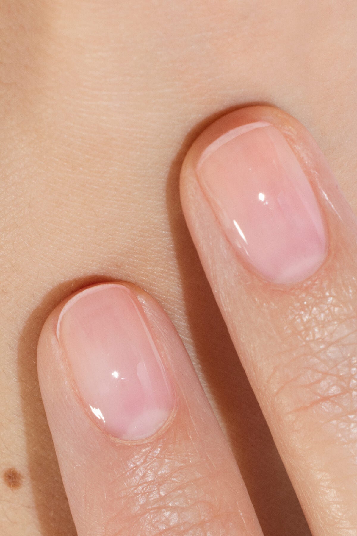 Gros plan de deux doigts aux ongles soigneusement coupés, vernis d’un vernis à ongles rose clair et brillant. La peau paraît lisse et les ongles ont un aspect naturel et sain.