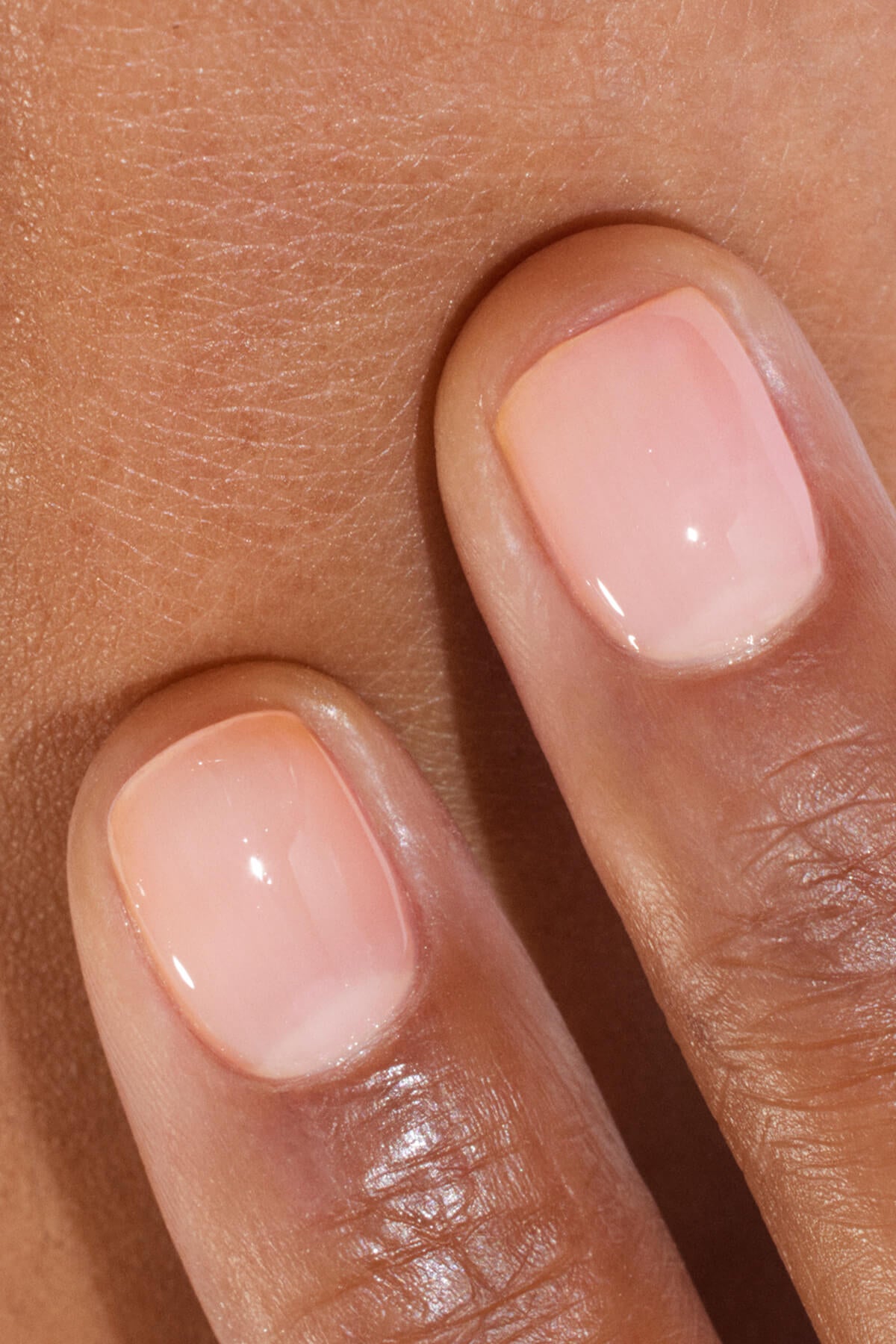 Gros plan sur deux doigts aux ongles soigneusement limés, vernis d'un rose pâle brillant et délicatement posés sur une peau mate.