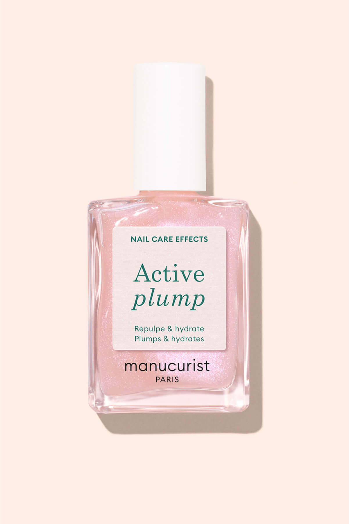 A bottle of Manucurist Paris Active Plump nail treatment with pink shimmery liquid, labeled Nail care effects. Active plump. Repulps  hydrates. Plumps  hydrates, on a pale pink background.