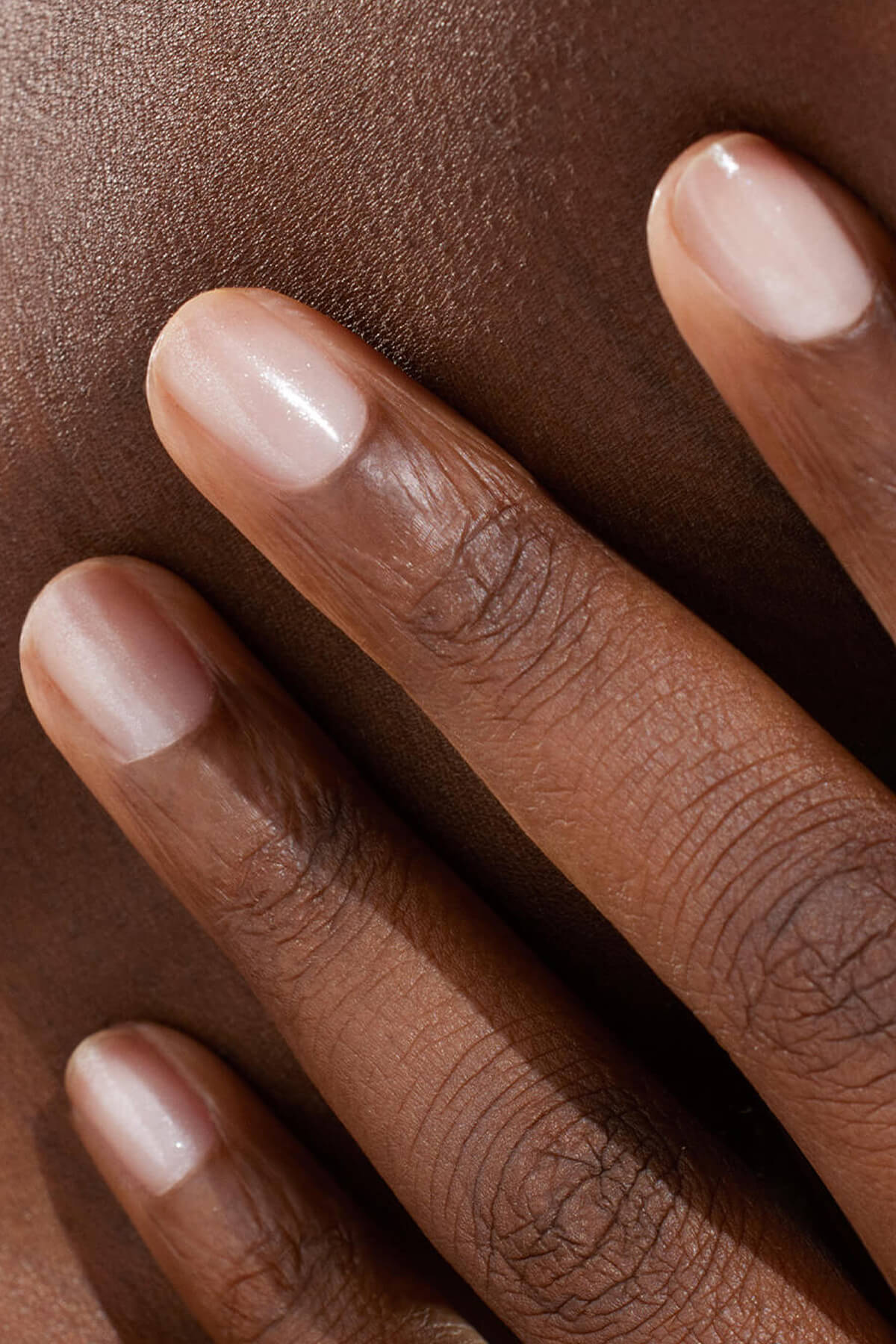Gros plan d'une main aux ongles courts et impeccablement manucurés posée délicatement sur une peau lisse et marron foncé. L'image met en valeur la texture et la carnation naturelles de la peau et des ongles.