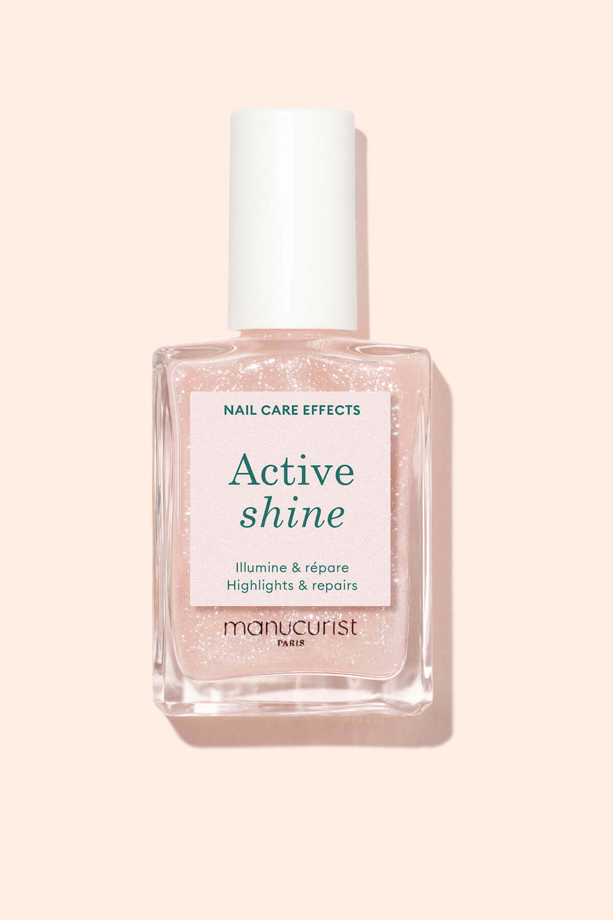 Un flacon de soin pour les ongles Active Shine Manucurist Paris avec un bouchon blanc, contenant un liquide rose clair scintillant. L'étiquette mentionne les bienfaits du soin, notamment l'effet illuminateur et la réparation.