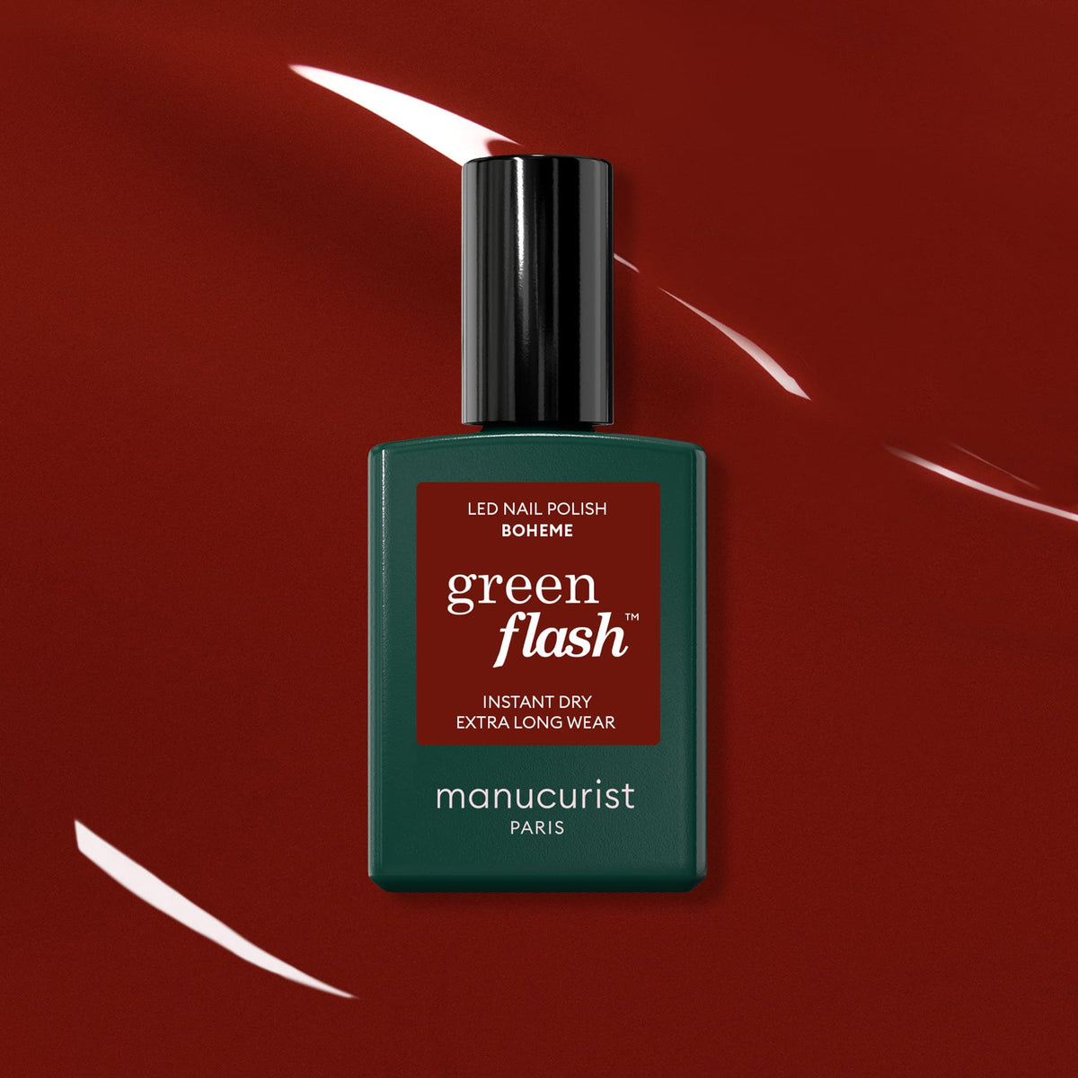 A bottle of Manucurist Bohème Green Flash LED polish—a Montmartre-inspired red-brown shade—rests on a glossy deep red surface with light reflections. The dark green bottle features a black cap and a red label.