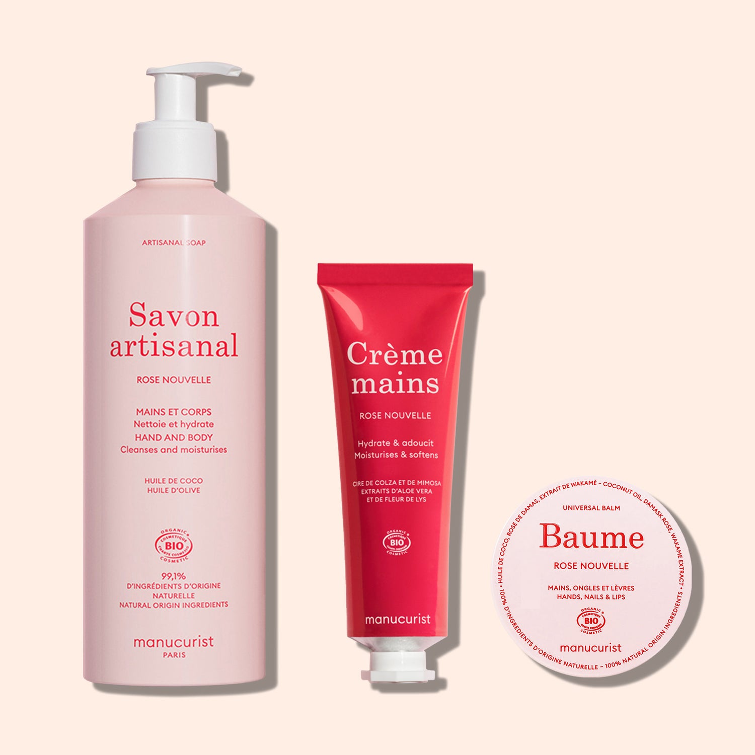 Three pink Manucurist containers—liquid soap, Everyday Rose Hand Cream – Cosmos Organic in a tube, and balm in a round tin—are displayed on a light pink background.