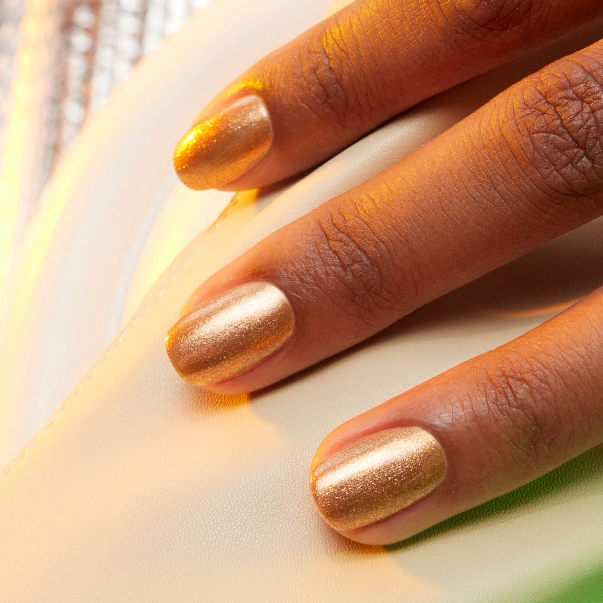 Gros plan d’une main posée sur une surface blanche, avec les ongles peints en Shimmer de Manucurist, un vernis à ongles bronze brillant effet miel glacé.