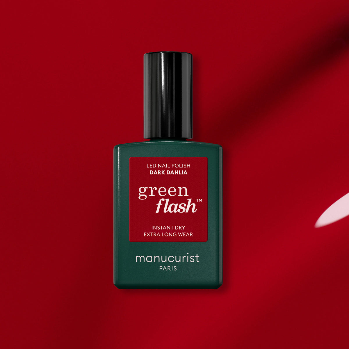Un flacon de vernis semi-permanent Manucurist Dark Dahlia est posé sur un fond rouge. Le flacon vert avec un bouchon noir et une étiquette rouge met en valeur la teinte intense de Dark Dahlia.