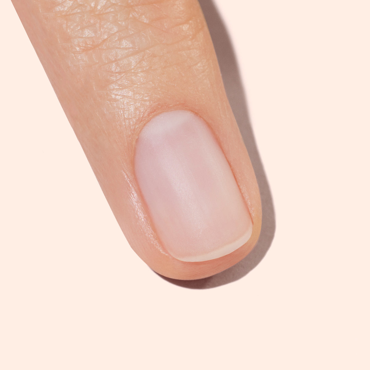 A close-up of a human finger with a neatly trimmed, clean, and natural fingernail against a light beige background.