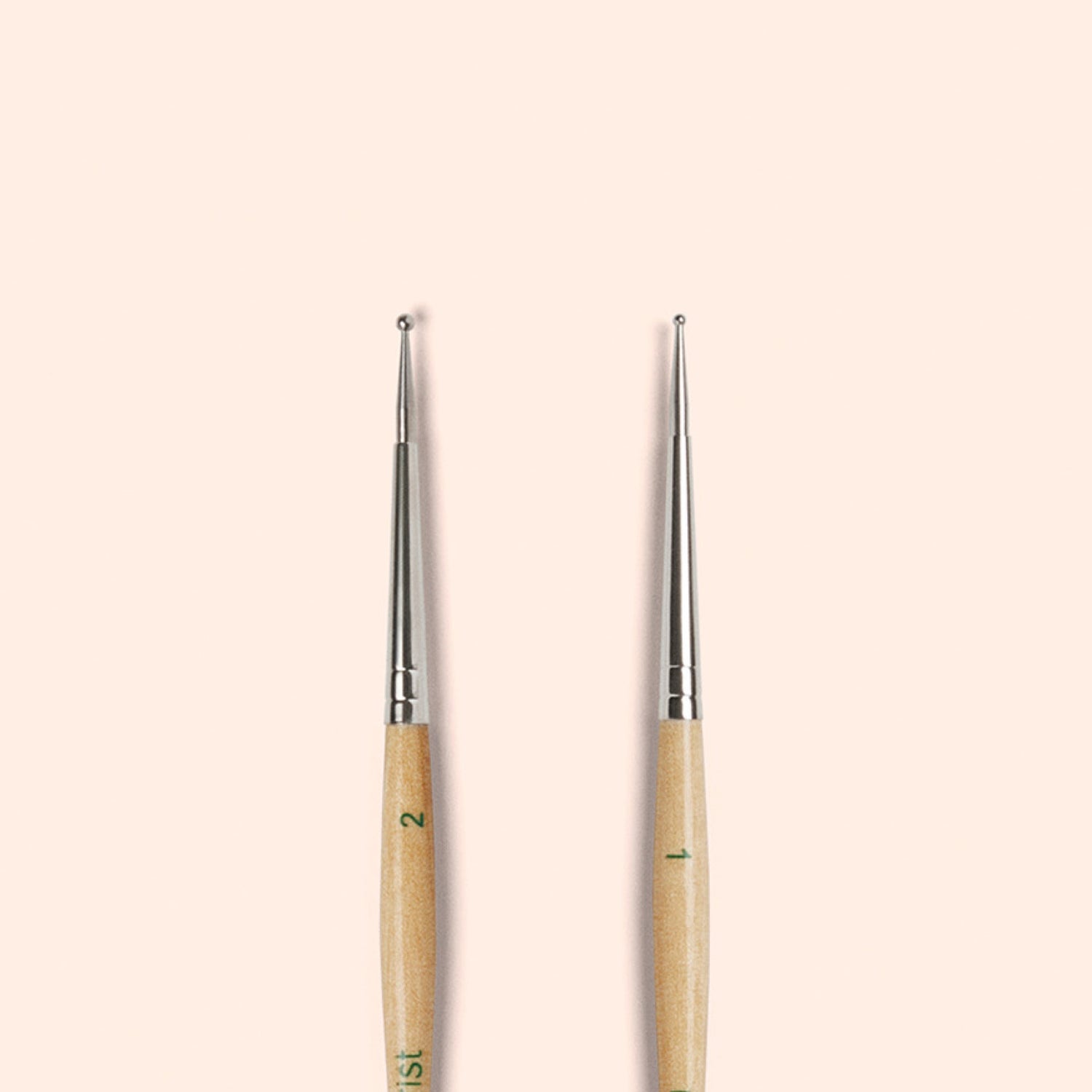 Two Manucurist Dotting Tools with metal tips and FSC wood handles are shown standing upright side by side on a light beige background, ideal for creating precise nail art designs.