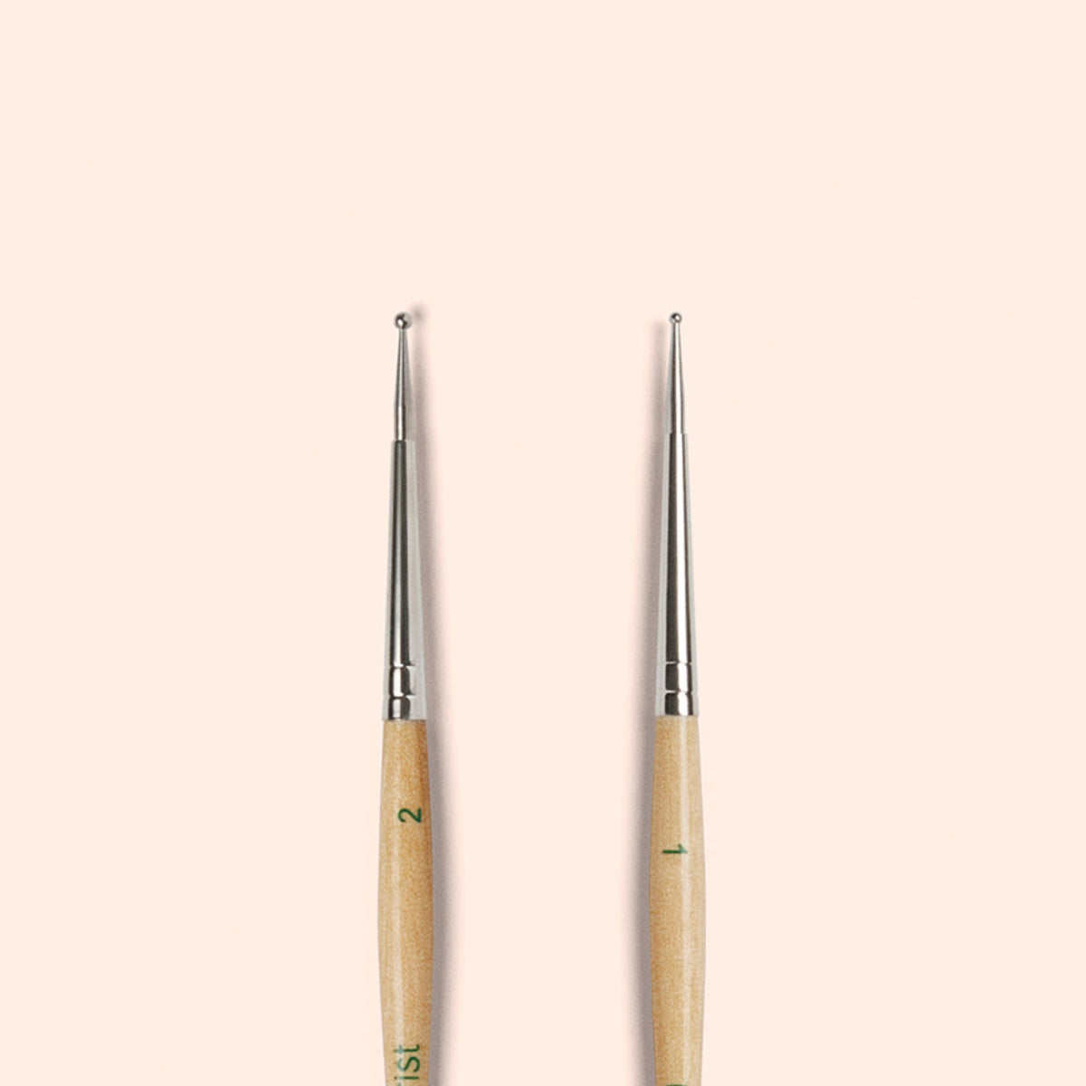 Deux Dotting Tools Manucurist avec embouts métalliques et manches en bois FSC sont présentés debout côte à côte sur un fond beige clair, idéaux pour créer des nail art précis.