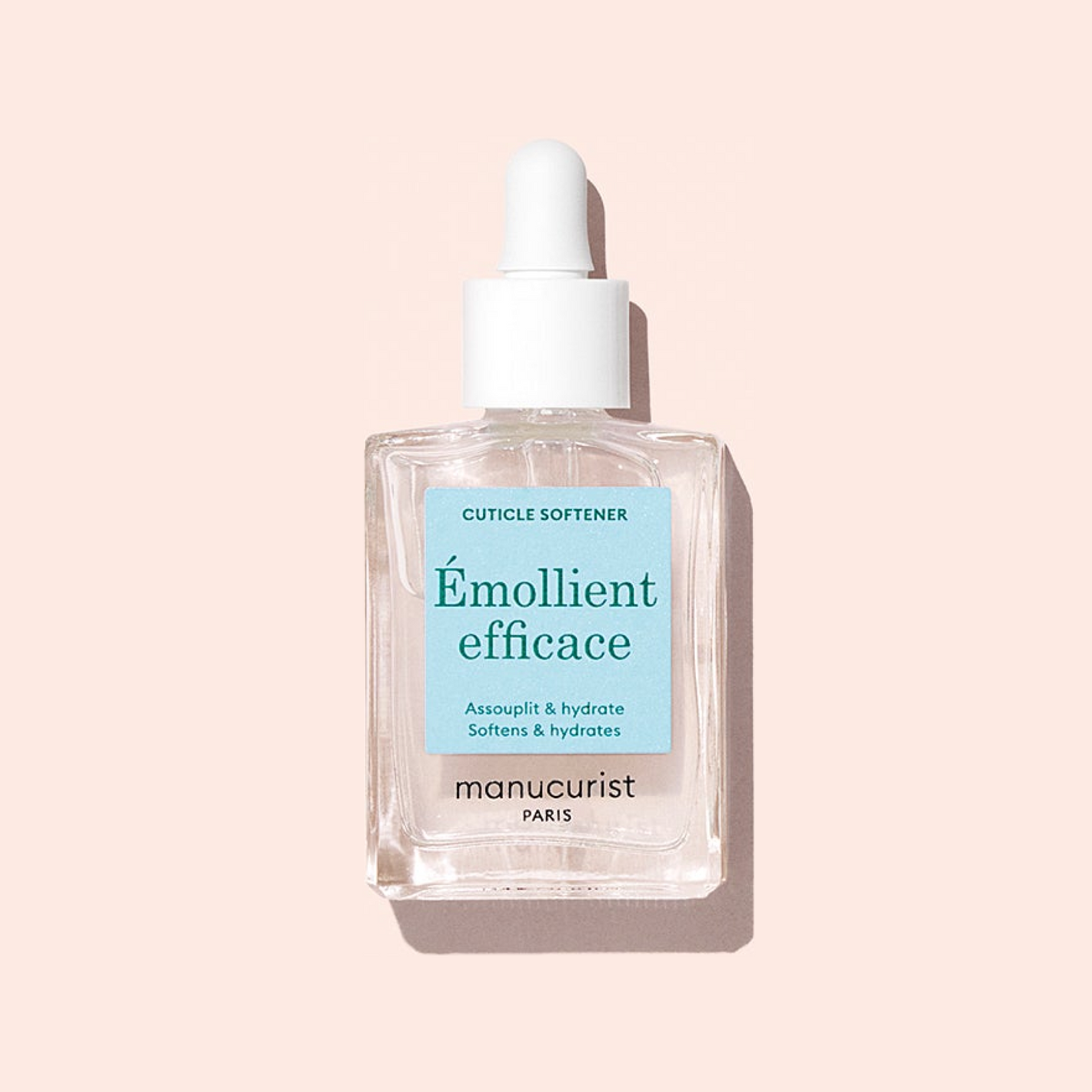 A clear glass bottle of Manucurist Hydrating Cuticle Softener with a white dropper cap and blue label reading "Émollient efficace," ideal for prepping nails before your manicure, is displayed against a pale pink background.