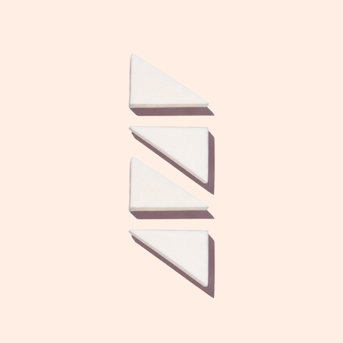 Four white, triangular Manucurist Nail Art Sponges are arranged vertically on a pale background, each casting a soft shadow to the right.