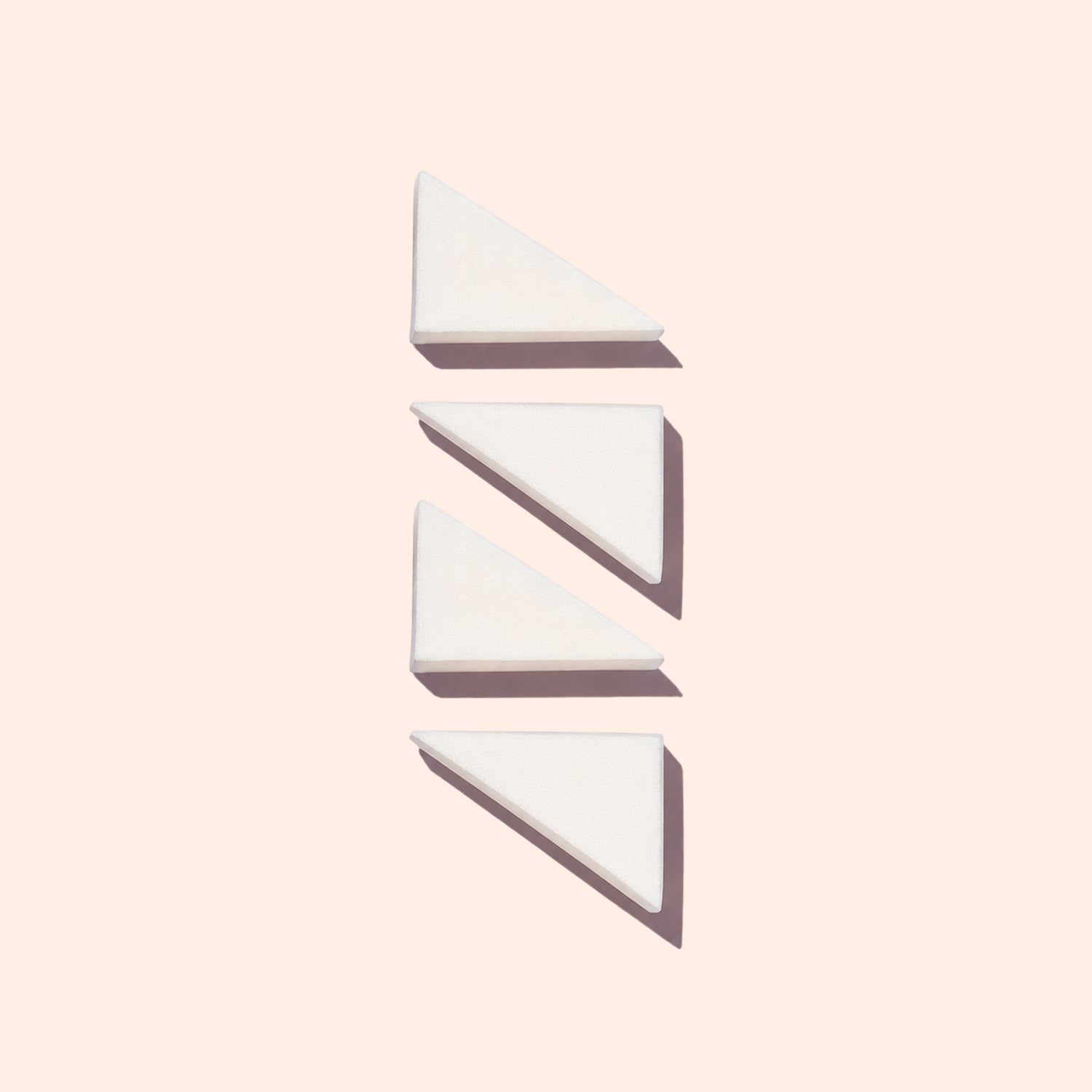 Four white, triangular Manucurist Nail Art Sponges are arranged vertically on a pale background, each casting a soft shadow to the right.