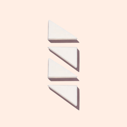 Four white, triangular Manucurist Nail Art Sponges are arranged vertically on a pale background, each casting a soft shadow to the right.
