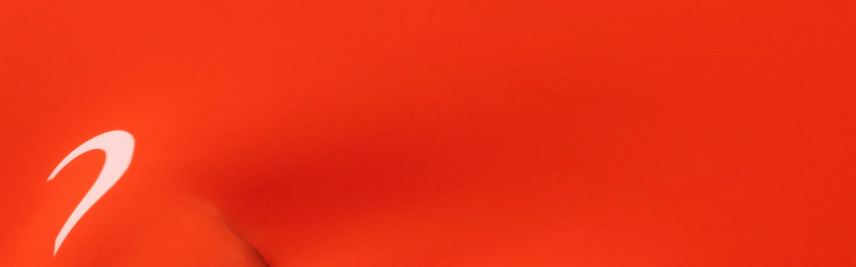 A close-up of a smooth, bright orange surface with a white swoosh logo in the lower left corner.